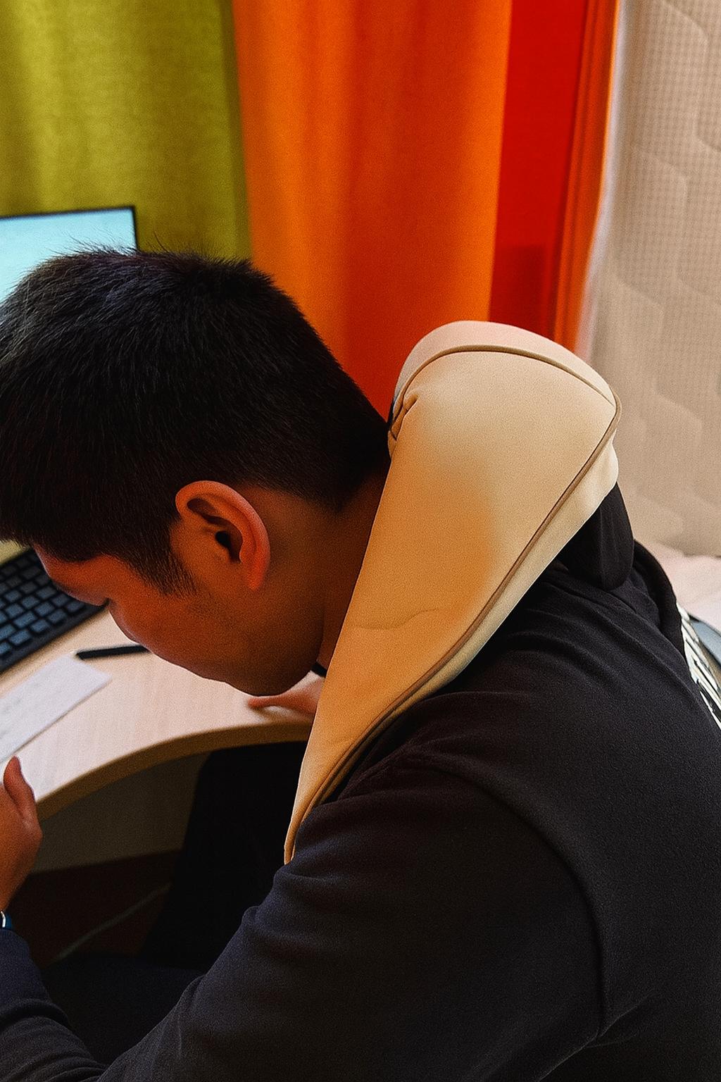 Person using a neck pillow at a desk with colorful curtains in the background