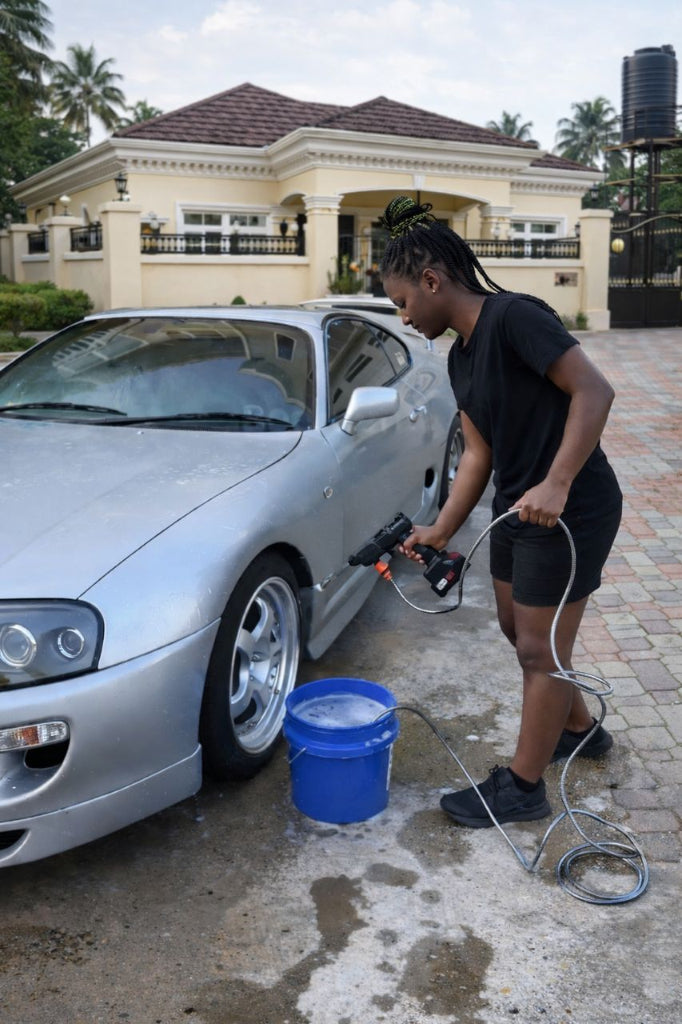 Person washing a silver car with a pressure washer in front of a house.