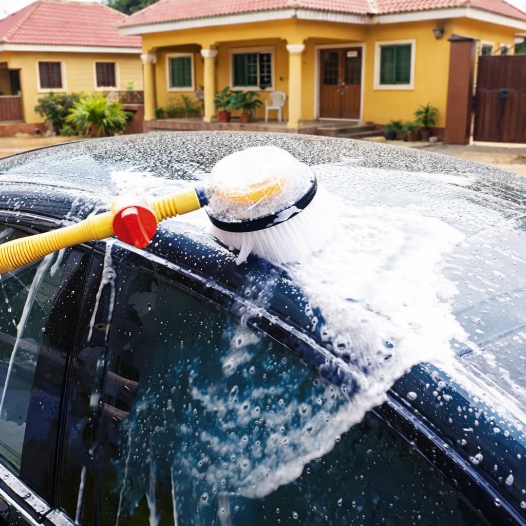 Car being washed with a sponge and water hose in front of a yellow house.