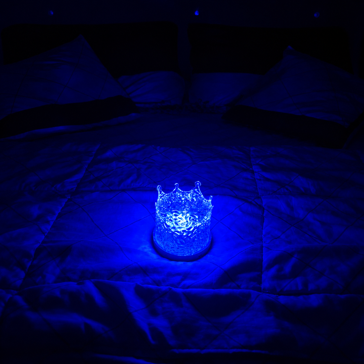 crown shape aurora galaxy projector glowing under a blue light on a bed
