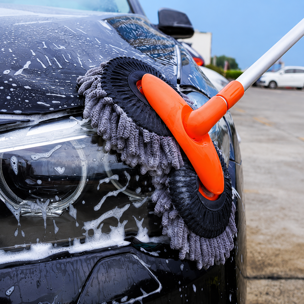 Car cleaning brush with gray bristle brush and orange handle on a car in a parking lot.
