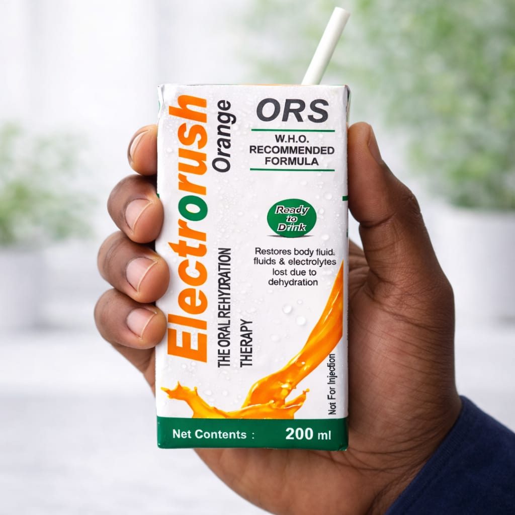 Hand holding a box of Electorush Orange ORS drink mix with a blurred green background