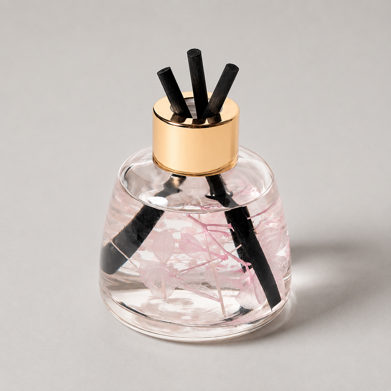 Clear pink glass diffuser with black reeds on a gray background