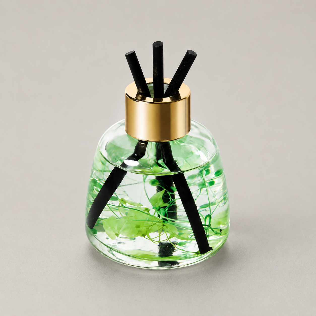 Clear green glass diffuser with gold cap and black reeds on a gray background