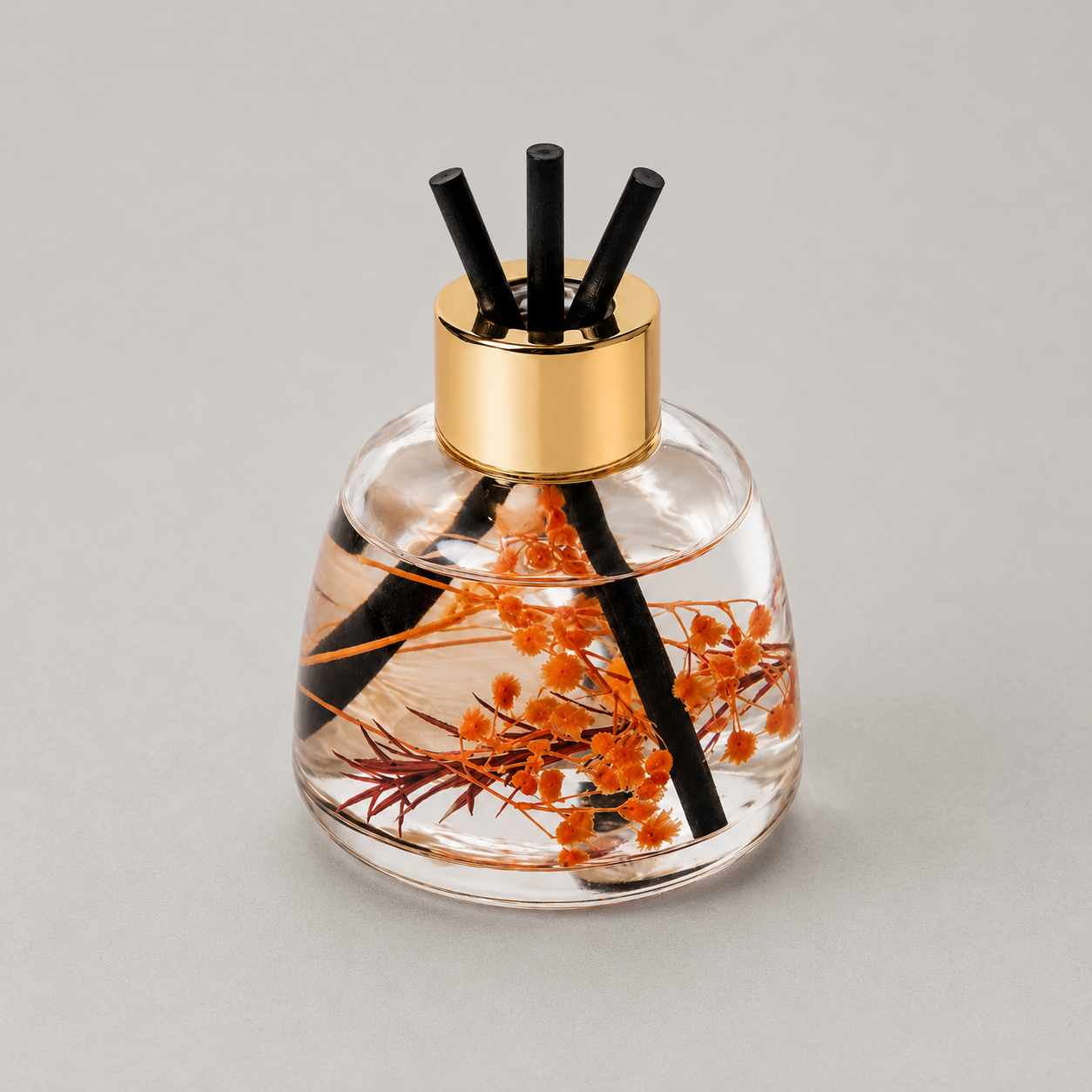 Clear gold diffuser bottle with black reeds on a gray background