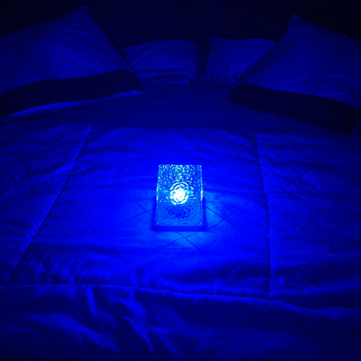 square shape aurora galaxy projector glowing under a blue light on a bed